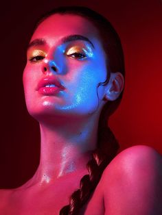 a woman with blue and pink light on her face is posing for a photo in front of a red background