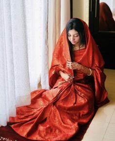 a woman sitting on the floor in a red dress looking at her cell phone while wearing jewelry