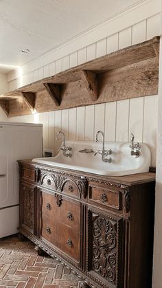 an old fashioned kitchen with wooden cabinets and white appliances in the corner, along with brick flooring