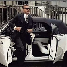 a man in a suit and sunglasses standing next to a car with its door open