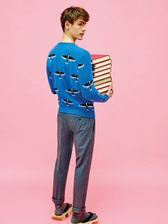 a young man holding a stack of books in front of his face while standing against a pink background