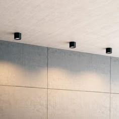 three lights on the side of a wall in an empty room with concrete walls and flooring