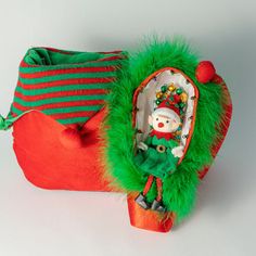 a green and red bag with a santa clause doll in it's pouch next to another bag