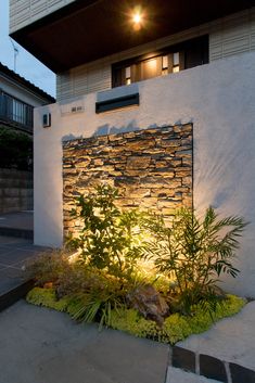 a house with a stone wall and plants in the front yard at night, lit up by street lights