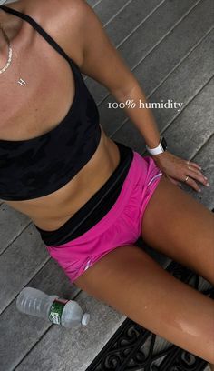 a woman in pink shorts and black top sitting on steps next to a water bottle