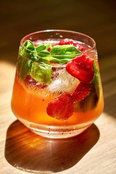 a close up of a drink on a table with strawberries and basil in it