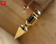 two gold colored objects hanging from a string on a wooden surface with wood planks in the background