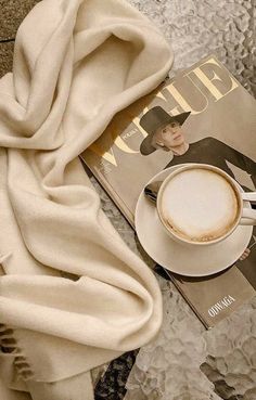 a cup of coffee sitting on top of a magazine next to a white scarf and hat