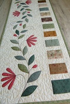 a quilted table runner with flowers and leaves painted on it's sides, sitting on a wooden floor