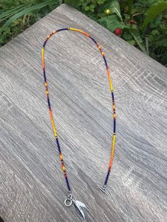 an orange, blue and yellow beaded necklace on a wooden surface with flowers in the background