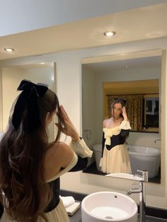 a woman standing in front of a bathroom mirror looking at herself in the mirror and brushing her hair