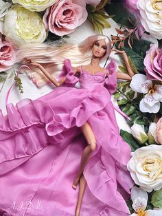 a barbie doll laying on top of flowers and wearing a pink dress with her hair blowing in the wind