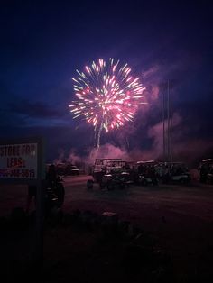 fireworks are lit up in the night sky over cars parked on the side of the road