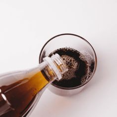 a glass filled with liquid sitting on top of a white table next to a bottle