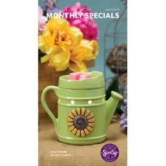 a green teapot with candles in it sitting on a table next to colorful flowers