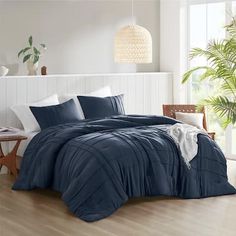 a bed with blue comforter and pillows in a room next to a plant on the floor