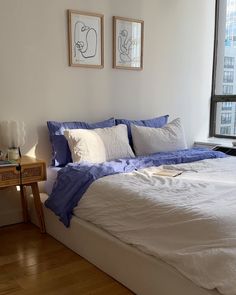 a bed with blue and white sheets in a bedroom next to a window, two pictures on the wall