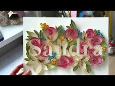 a hand holding up a card with flowers on it that says sendra in large letters