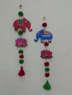 two colorful ornaments are hanging on a white wall with red and green tassels