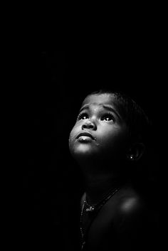 a black and white photo of a young boy looking up at something in the dark