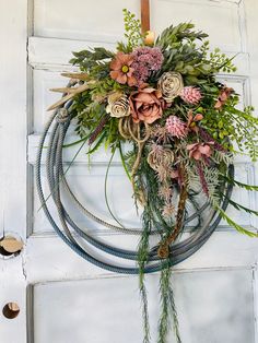 a wreath hanging on the door with flowers and greenery attached to it's sides