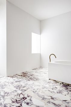 an empty bathroom with marble flooring and white walls, along with a gold faucet