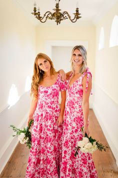 two beautiful women standing next to each other in pink and white dresses holding bouquets