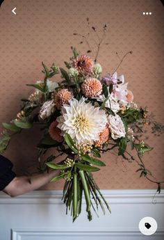 a person holding a bouquet of flowers in front of a wall with pink and white flowers