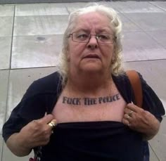 an older woman with tattoos on her chest standing in front of a parking meter and looking at the camera