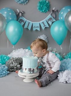 a baby boy sitting in front of a cake with blue and silver decorations on it