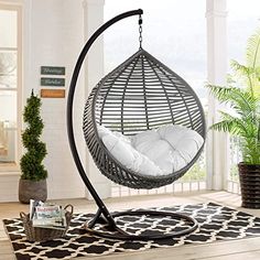 a hanging chair with pillows on it in the middle of a room next to a potted plant