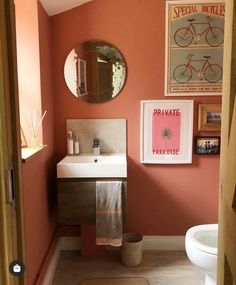 a bathroom with pink walls and pictures on the wall above the toilet, sink and mirror