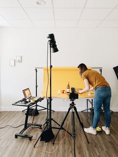 a woman standing in front of a camera on top of a wooden floor next to a yellow screen