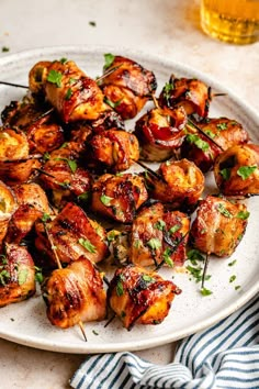 chicken skewers on a white plate next to a glass of beer