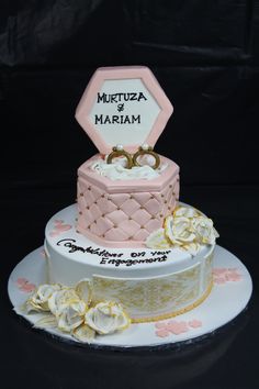 two tiered cake decorated with pink and white frosting, topped with gold rings