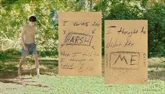 two signs with words written on them in the grass next to a man standing by some trees