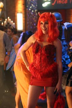 a woman with red hair wearing a costume and posing for the camera in front of other people