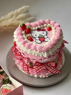 a hello kitty cake with strawberries on top and a box of chocolates in the background