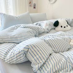 an unmade bed with blue and white striped comforter, pillows and stuffed animal