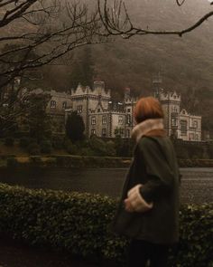 a woman standing in front of a large building on top of a lush green hillside