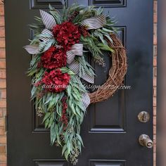 a wreath with red flowers and greenery hangs on the front door's black door