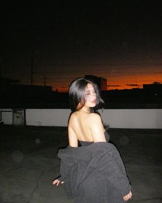 a woman sitting on top of a roof next to a building at night with the sun setting in the background