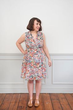 a woman standing in front of a wall with her hands on her hips, wearing a floral dress