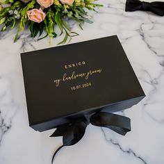 a black box with gold lettering on it sitting on a marble surface next to flowers