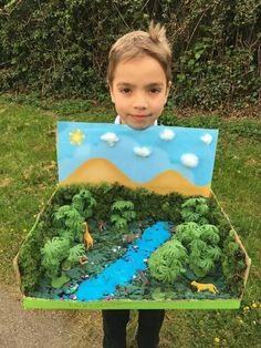 a young boy is holding up a cardboard box with an image of a river in it