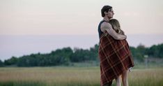 a man and woman wrapped in a blanket standing next to each other with trees in the background