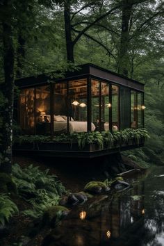 a small cabin in the middle of a forest next to a pond with lights on it