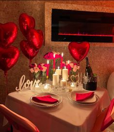 a table set for valentine's day with candles and heart shaped balloons