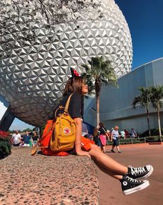 a woman sitting on the ground in front of a building with a large ball behind her