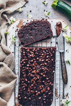 two slices of chocolate zucchini bread on a cooling rack next to a knife